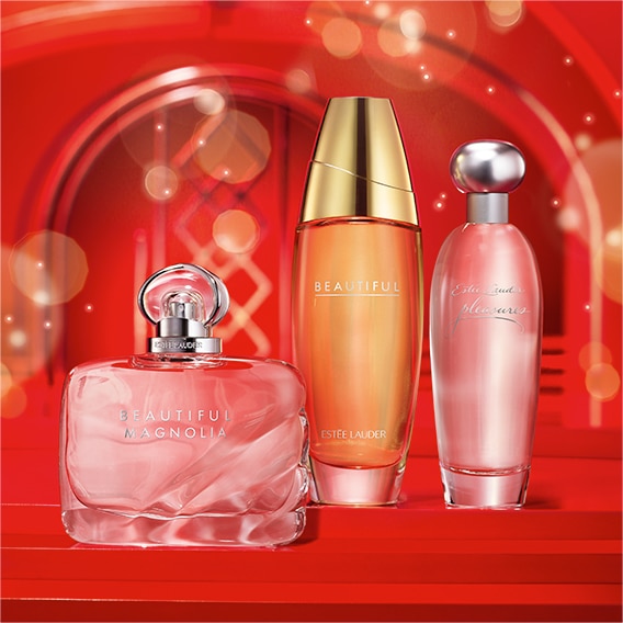 3 Estee Lauder fragrances lined next to each other with a red holiday background